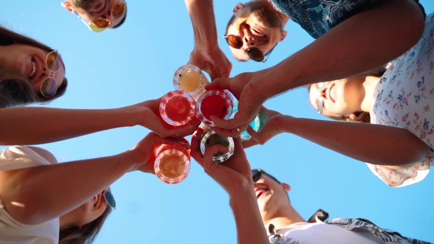Low angle view of friends having fun at pool party, clinking glasses with colorful summer cocktails near hotel swimming pool. People toast drinking fresh juice at luxury summer villa in slow motion. | Shutterstock HD Video #1051142527
