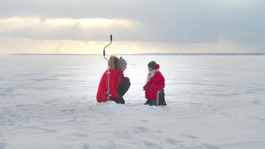 Dad and son are fishing in the winter. Long shot