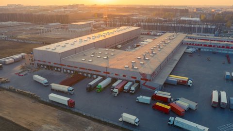 Aerial hyper lapse (hyperlapse - time lapse) of the large logistics park with warehouse, loading hub and semi trucks with cargo trailers standing at the ramps for load/unload goods at sunset