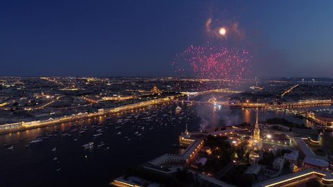 Aerial sideways St. Petersburg festive salute firework over Peter and Paul fortress. Night downtown historical cityscape illumination. Neva river many ships. Road traffic embankment. Day of city