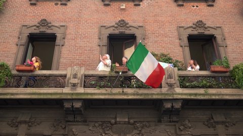 Italy, Milan April 25, 2020 People on the balconies sing Bella Ciao the day of the Resistance during covid 19 Coronavirus quarantine at home - Italian flash mob and flag - family mother and father 