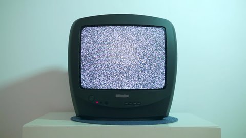 Old TV 90-2000 years old, stands on a white nightstand and shows the noise of the screen. Damage to the video signal with pixel noise and noise. 