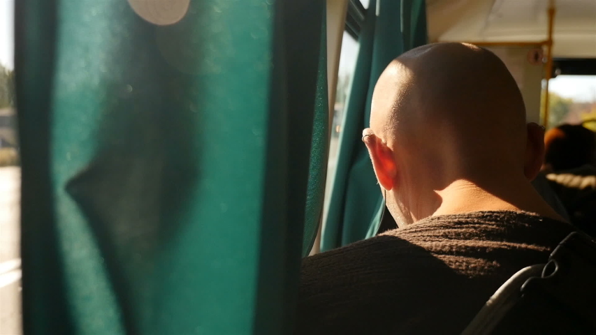 Bald man riding on a bus. Sunlight in the window. Close-up