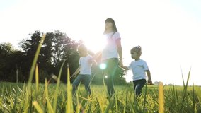 happy family teamwork mother, little brother and sister walk in the park nature holding hands slow motion video concept. mom, kids boy and girl daughter and son hold lifestyle hands go on green grass