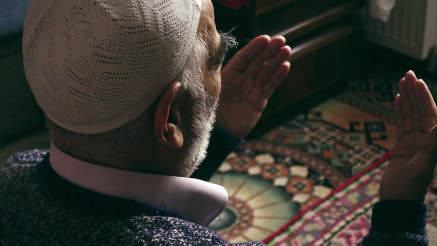Elderly Turkish muslim man wearing prayer cap prays to Allah by raising his hands at his home on his prayer rug in Ramadan month | Shutterstock HD Video #1051187914