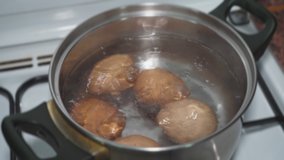 Chicken eggs are boiled in the metal pan in water on a gas stove