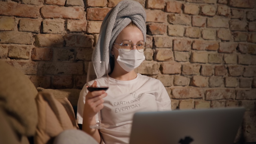 Cute woman holds red wine and looks at camera with laptop and cat at home