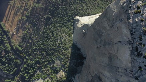 Aerial top-down shot of a densely forested valley at the foot of the massive granite rock El Capitan in Yosemite National Park. Vertical smooth walls of the mountain rise high over the valley. 4K