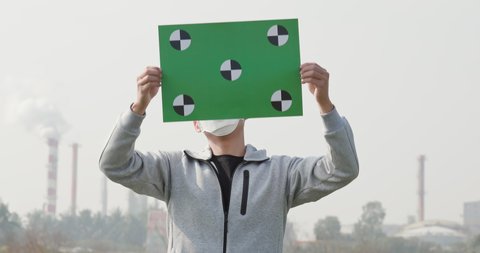 asian man hold green copy space billboard and wears protective n95 mask against air pollution standing in front of factory