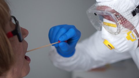 Coronovirus test, test for determining coronovirus infection. Close up Microbiologist in a protective suit takes a sample of biomaterial from the oral cavity of an elderly woman