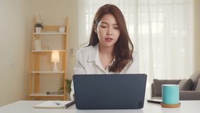 Asian businesswoman using laptop talk to colleagues about plan in video call while smart working from home at living room. Self-isolation, social distancing, quarantine for coronavirus prevention.