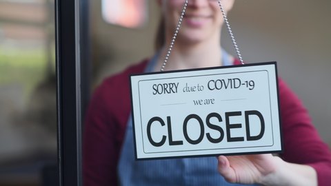 Small business owner smiling while turning the sign for the reopening of the place after the quarantine due to covid-19. Close up of woman’s hands holding sign now we are open support local business.