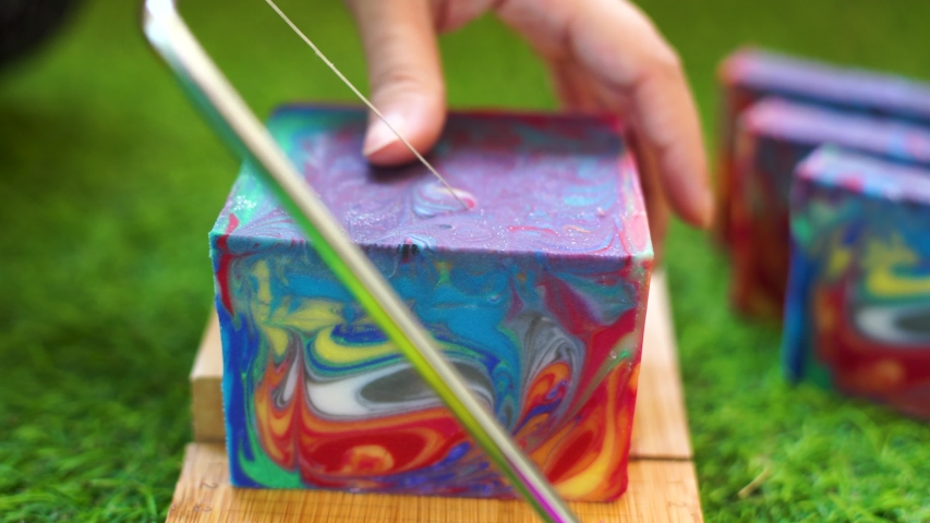 Woman using a wire cutter to cut bars from a colorful loaf of home made hand made soap on grass signifying the natural oils and ingridients used by hobby home and small business makers. Shows the very Royalty-Free Stock Footage #1051200949