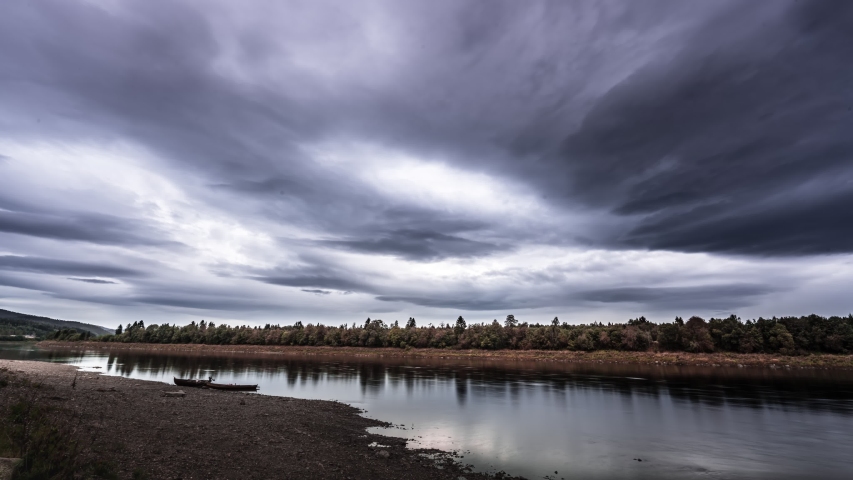 Gray gloomy clouds flowing over the Namsen river. Calm waters, boats waiting on the shore.