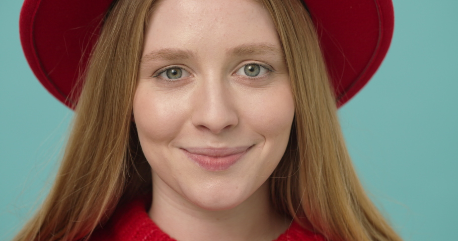 
Pretty young woman with long blond hair in a red hat winking smiling looking at the camera isolated over blue background.
