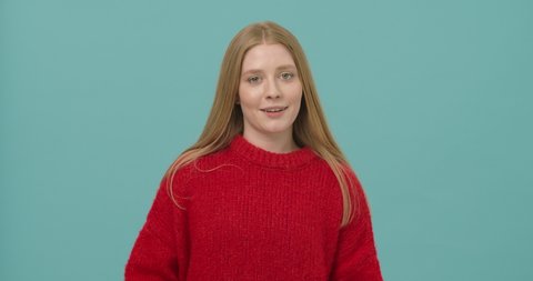 
Smiling young woman with long blond hair dressed in a red sweater disingenuously showing fuck you gesture isolated over blue background. Fuck you gesture