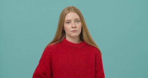 Annoyed young woman with long blond hair dressed in a red sweater showing fuck you gesture with two hands isolated over blue background. Concept of anger and irritation