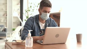 Work from home isolation coronavirus pandemic, Covid 19 quarantine. A young man uses a medical mask and a hand sanitizer to protect himself. He works on a laptop. Stay self isolation at home - Powered by Shutterstock - Get 15% off with code: PIKWIZARD15