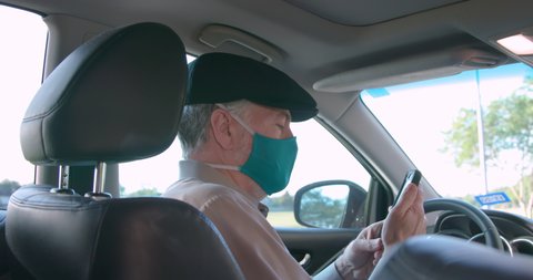 A mature retiree Uber or Lyft ride sharing driver wearing a mask due to COVID19 risks greets his passenger and engages in friendly conversation before starting the ride.