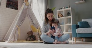 Young modern caucasian vlogger mom is showing her smartphone to little daughter, playing games with her or showing cartoons - family activity, technology concept 4k footage
