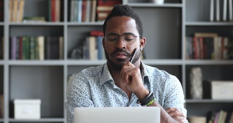 Head shot pensive young biracial man looking at laptop screen, thinking of hard problem decision or case study. Thoughtful mixed race entrepreneur businessman employee stack with difficult task.