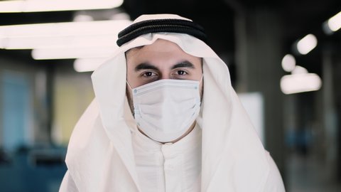 Arab businessman in kandura takes off medical mask. Male breathes deeply and smiling looking at camera. Medical concept. Close up portrait . 4k
