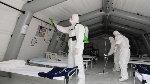 Cremona, Italy - March 20, 2020: Men wearing PPE protective gear disinfect inside a tent of Samaritans's Purse field hospital before the arrival of patients affected by Covid-19 Coronavirus