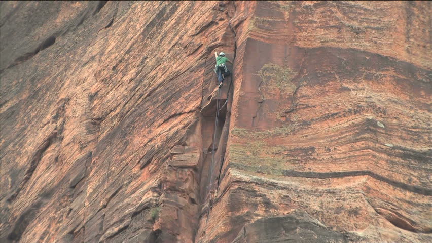 Rock Climber repelling down a 200 foot rock face in Zion National Park Utah