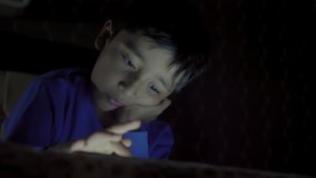 A young child/ kid/ male using a creative painting app on a tablet or mobile phone while lying on the bed. A intelligent/ focused boy busy playing online video games on smartphone in the dark. 