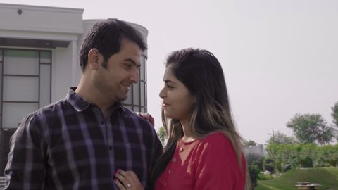 A happy and smiling couple holding each other standing in front of their dream home. A married husbandwife outside the newly constructed bungalow looking at the camera with a smile. 