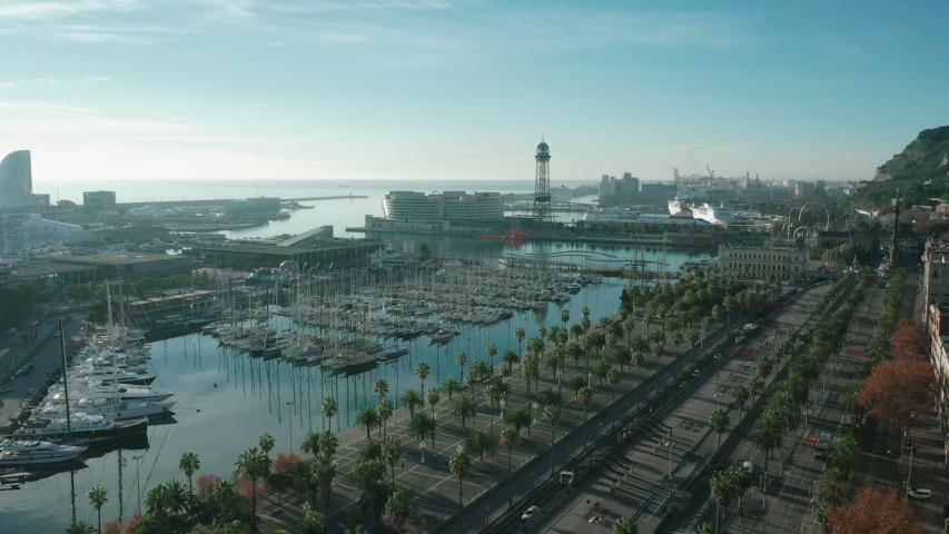 Aerial view of city port in Barcelona; parking for large luxury yachts in touristic capital of Catalonia; sunny day in Barcelonetta, sailboats, hotels, old buildinags illuminated by warm morning sun Royalty-Free Stock Footage #1051250509
