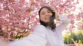 Beautiful woman having video chat using smartphone outdoors sharing travel adventure friends showing sakura blossom. Girl filming selfie video photo for social media. Japan vacation slow motion
