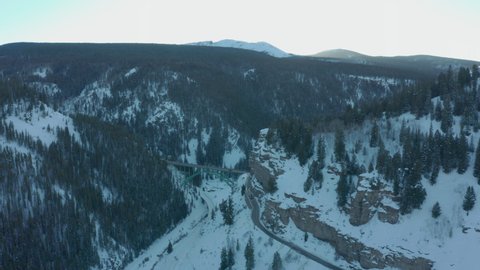 Aerial Drone Shot Approaching Scenic Green Bridge Over Snowy Mountain Valley