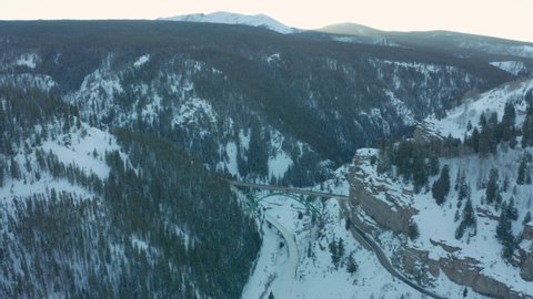 Aerial Drone Shot Flying Over Scenic Green Bridge Over Snowy Mountain Valley