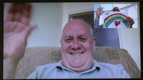 Social distancing. Happy senior elder man on webcam camera video chat call at home, recording vlog. Son NHS rainbow drawing. Self isolation coronavirus, covid pandemic. London, England, UK. 26/04/2020