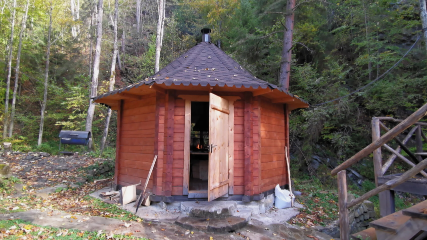 A wooden cabin is a kitchen with burning fire in it for tourists use next to a wooden hand made platform over a small mountain river. Holidays in the Carpathian mountains, Ukraine. Prores 422