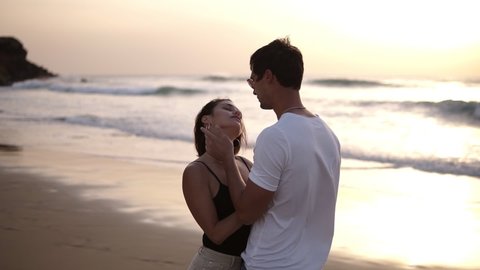 Young couple kissing and bonding at sunset on beach. Loving man and woman hugging in bright rays of sun on background of the lake. Passioned guy and girl in love