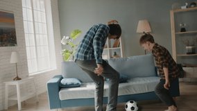 Happy father and son playing football together at home. Caucasian man dribbling the ball while young son tries to take it from him - active games, happy family concept 4k footage