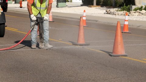Dust flies from the machine as a man laborer works with a jackhammer on the asphalt of a city street as part of a utility project. Slow motion clip.
