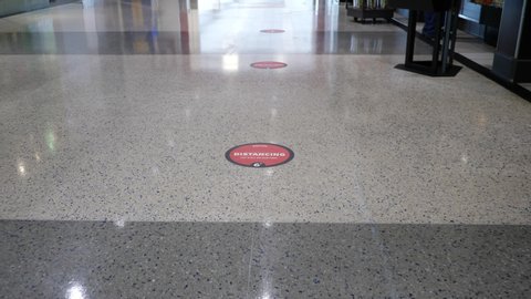 Social distancing stickers "Let's all do our part" spaced 6 feet apart on a shiny floor at the airport to help customers queue safely