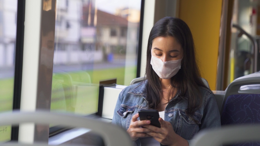Young woman in protective medical face mask in a subway car on her mobile. Pandemic coronavirus concept

