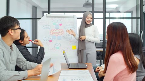 Asian muslim woman lead group of young Asian business creative team in brainstorm meeting presentation. Girl power, colleague coworker partnership teamwork, people cooperation, or idea sharing concept