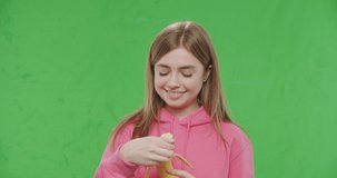 close up portrait of young woman biting big fresh ripe banana over chroma key background. Sporty girl in pink hoodie on green screen. 4k raw footage video slow motion