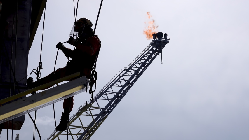 Working at height. Silhouette of abseiler team hanging at the edge oil and gas platform for maintenance works with background flare tip boom burning. Royalty-Free Stock Footage #1051286590