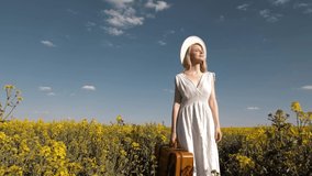 Beautiful woman in dress with suitcase in rapeseed field