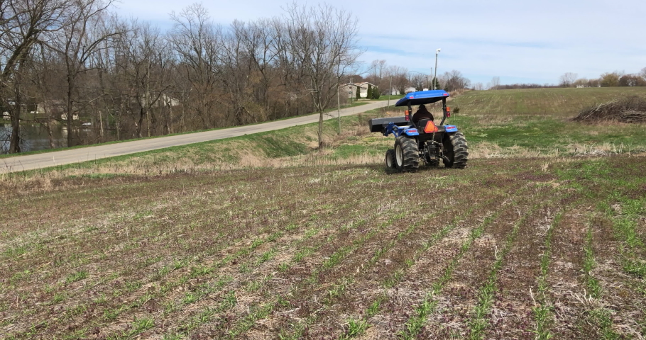 Farmer on tractor dumps rocks in field 