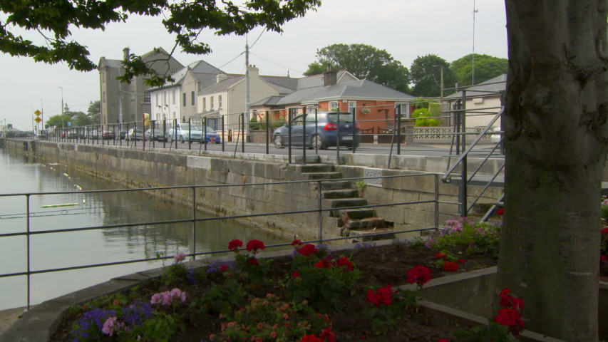 Lockdown shot of vehicles on street amidst canal and buildings in city against sky - Galway, Ireland