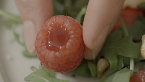 Close-up slow motion shot of woman holding fresh raspberry while preparing on salad in kitchen - Paris, France