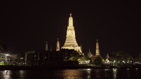 Panning shot of illuminated Buddhist temple by river in city against sky at night - Bangkok, Thailand