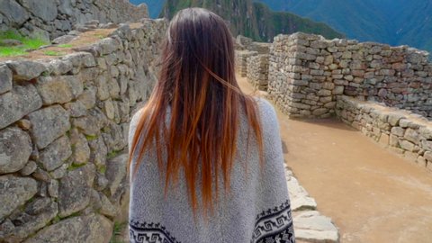 Slow motion of young woman wearing poncho walking amidst old ruins against mountains - Machu Picchu, Peru